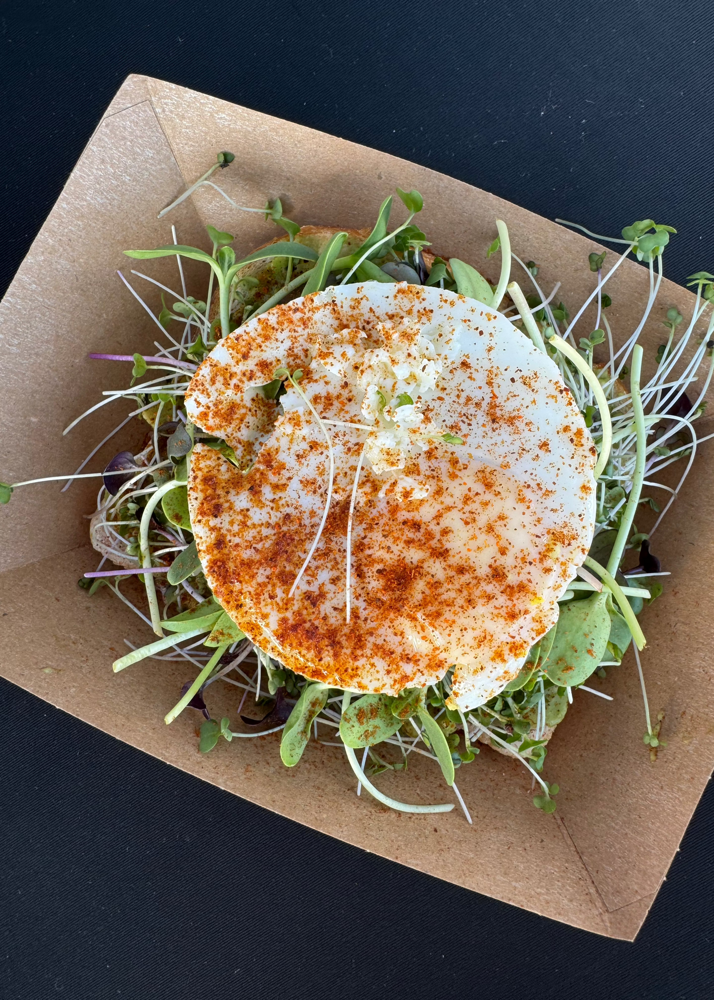 Avocado toast topped with microgreens on rustic bread, served on a white plate with natural lighting.