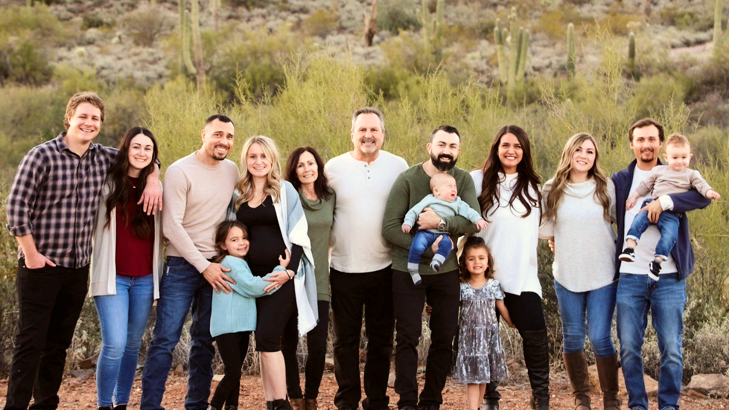 Large extended family smiling together outdoors in a desert landscape with cacti in the background.